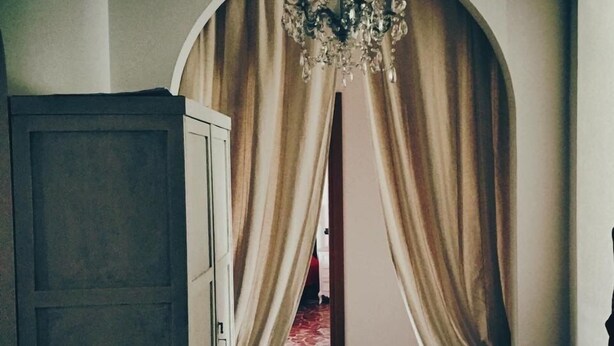 An arched doorway with heavy drapes, a chandelier, and a wooden wardrobe. - Domus Mea- Adults Only (Verona)
