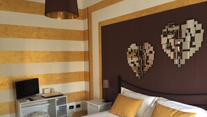 A hotel room with a bed, a desk, a television, and a wall with heart-shaped decorations. - Domus Mea- Adults Only (Verona)