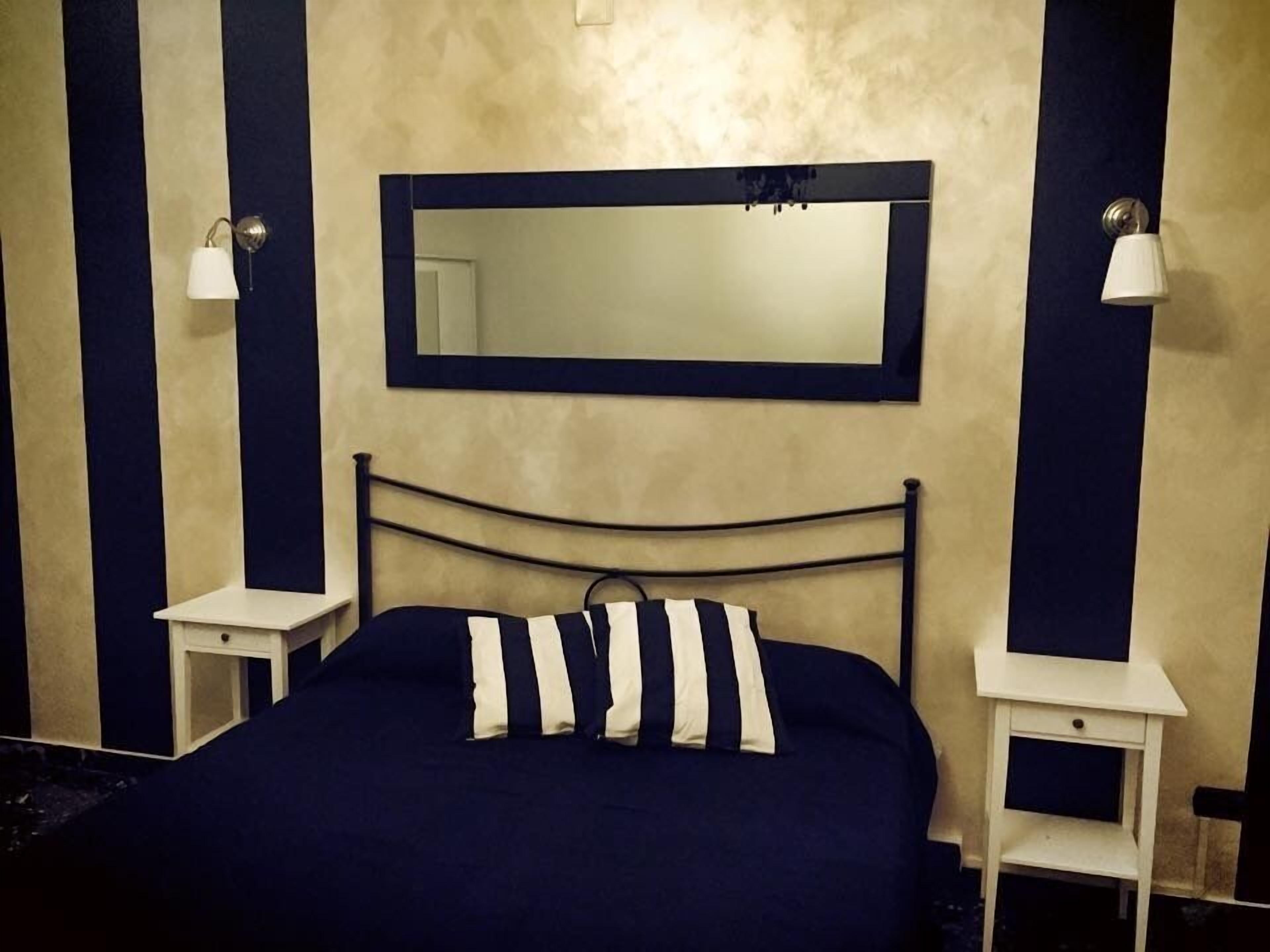 Un dormitorio con una cama, un espejo grande, dos mesitas de noche y una mesita auxiliar.