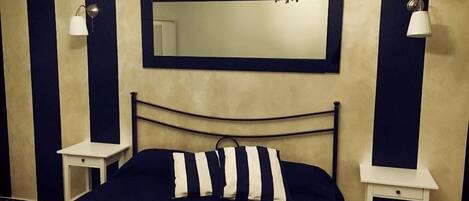 Un dormitorio con una cama, un espejo grande, dos mesitas de noche y una mesita auxiliar.