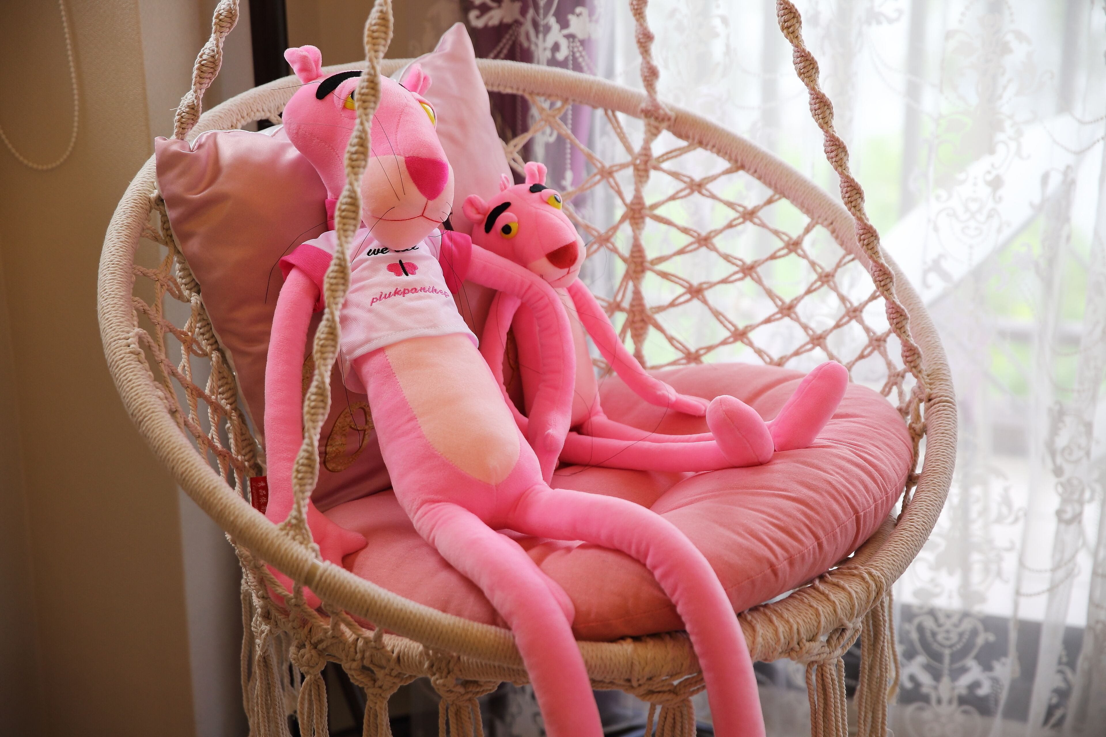 A wicker hanging chair with pink cushions and plush toys.