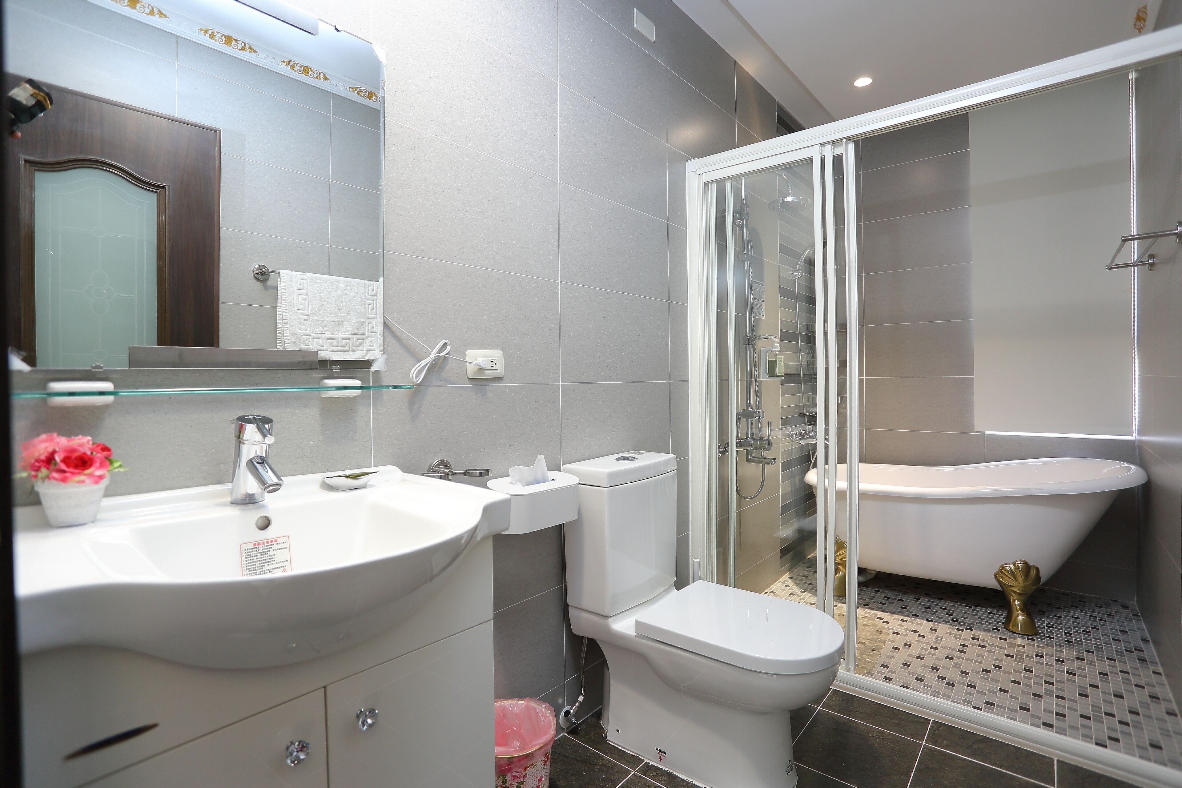 Un baño moderno con ducha envuelta en vidrio, una bañera independiente y un lavamanos blanco con encimera de cristal.