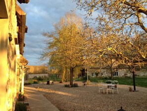 A courtyard with a stone building, a large tree, and outdoor seating. - La Ferme des Isles (Autheuil-Authouillet)