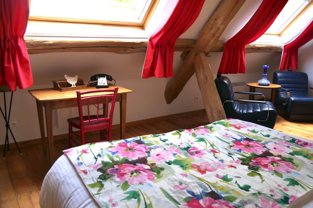 A bedroom with a bed, a desk, a chair, and a window with red curtains.