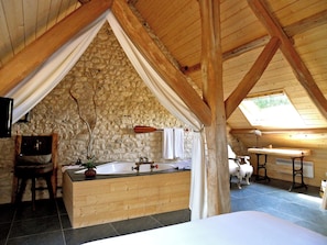 A rustic bathroom with a stone wall, wooden beams, a bathtub, and a wooden counter. - La Ferme des Isles (Autheuil-Authouillet)