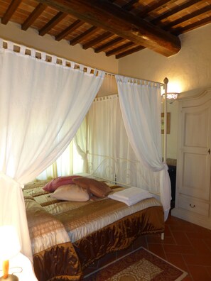 A bedroom with a bed, white curtains, a wooden ceiling, and a tiled floor. - Fattoria di Colleoli (Palaia)