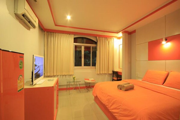 Una habitación de hotel con una cama, un escritorio con una computadora, una ventana con cortinas y un televisor sobre el escritorio.