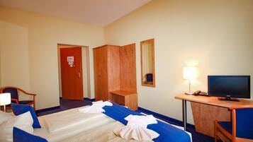 Een hotelkamer met twee bedden, een bureau met een computer, een stoel, een kledingkast en een spiegel.