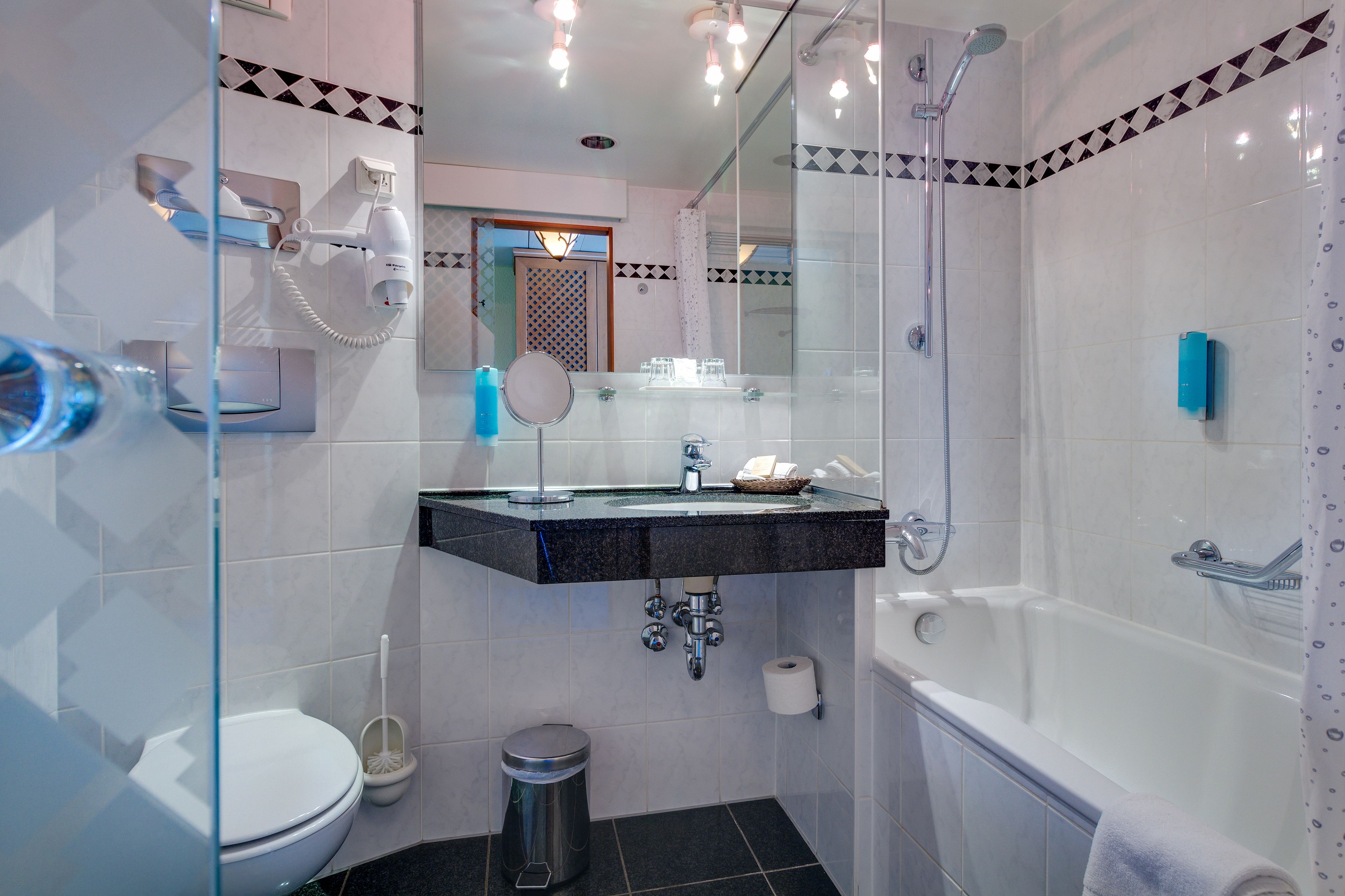 Un baño moderno con cabina de ducha de vidrio, un lavabo con espejo, inodoro y un cubo de basura.