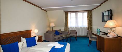 A hotel room with a large bed, a desk, a chair, a sofa, and a TV.