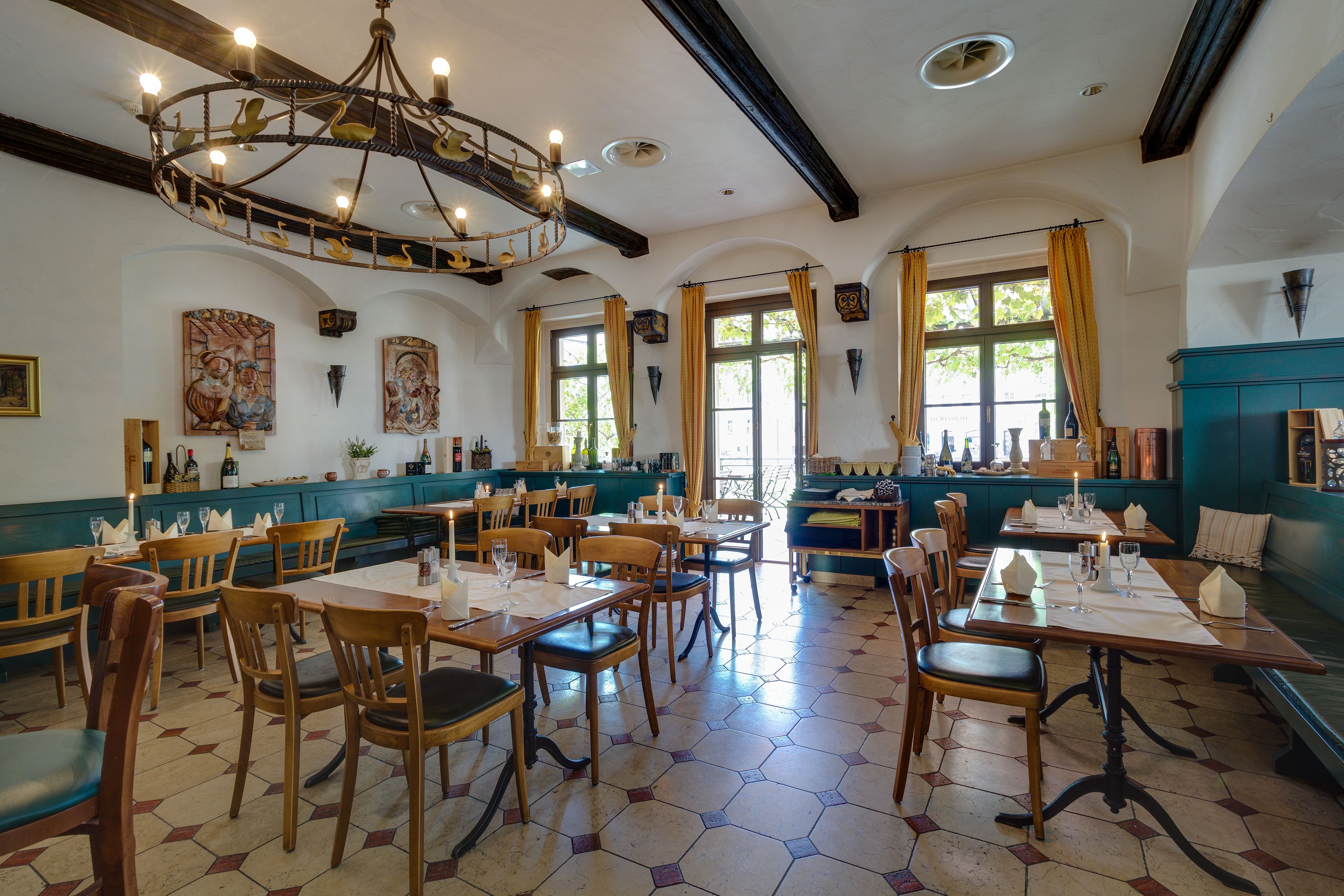 Een restaurant met hexagonaal patroon in de vloer, houten tafels en stoelen, en een kroonluchter met hangende verlichtingsarmaturen.