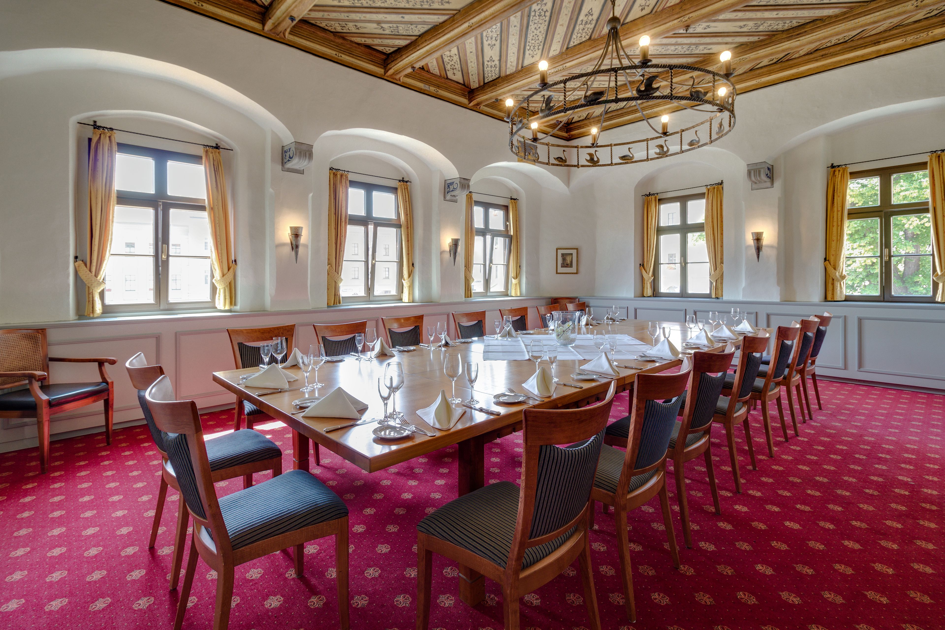 Una sala de menjador amb un gran taulell preparat per a dinar, envoltat de cadires, finestres d'arc i un penjall.