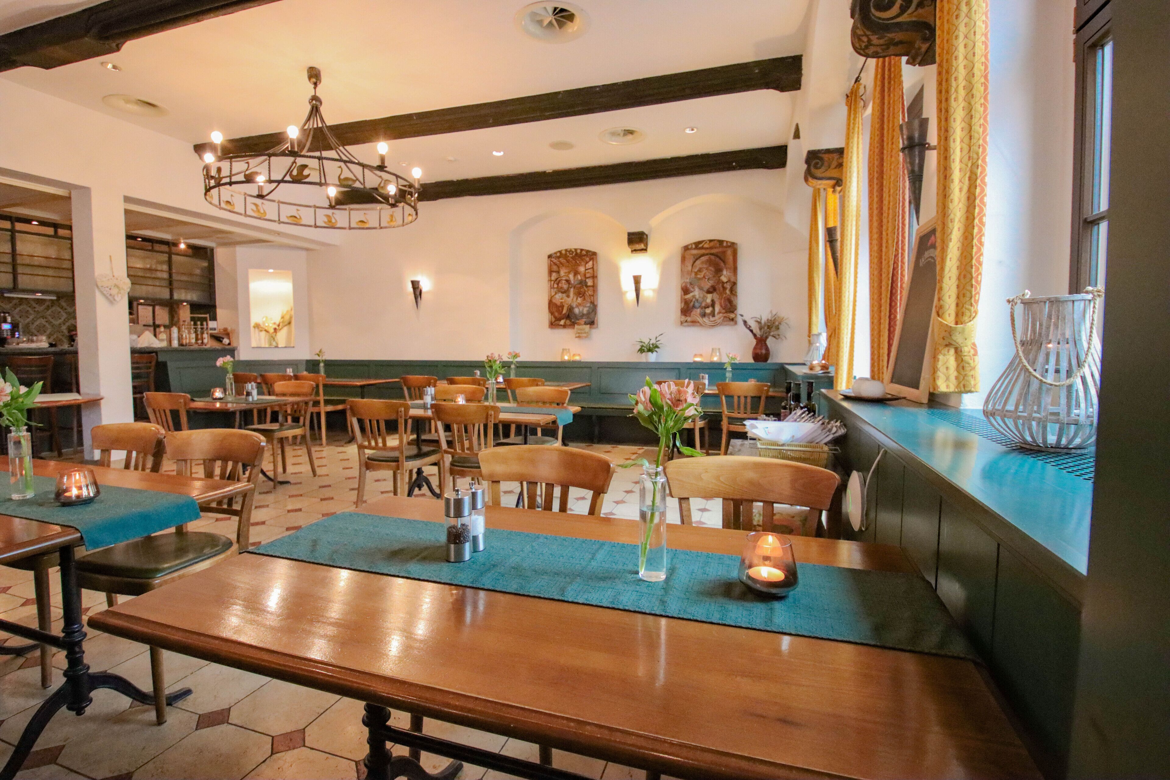 A restaurant with wooden tables and chairs, a chandelier, and artwork on the walls.