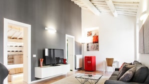 A modern living room with a flat-screen TV, a red refrigerator, a glass coffee table, and a grey sofa. - At Home Spanish Steps (Rome)
