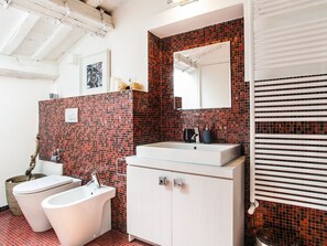 Une salle de bain moderne avec un mur recouvert de mosaïques rouges, un lavabo blanc, une baignoire et des toilettes.