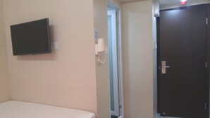 Una habitación de hotel con una cama, un televisor montado, una puerta y un secador de manos en la pared.