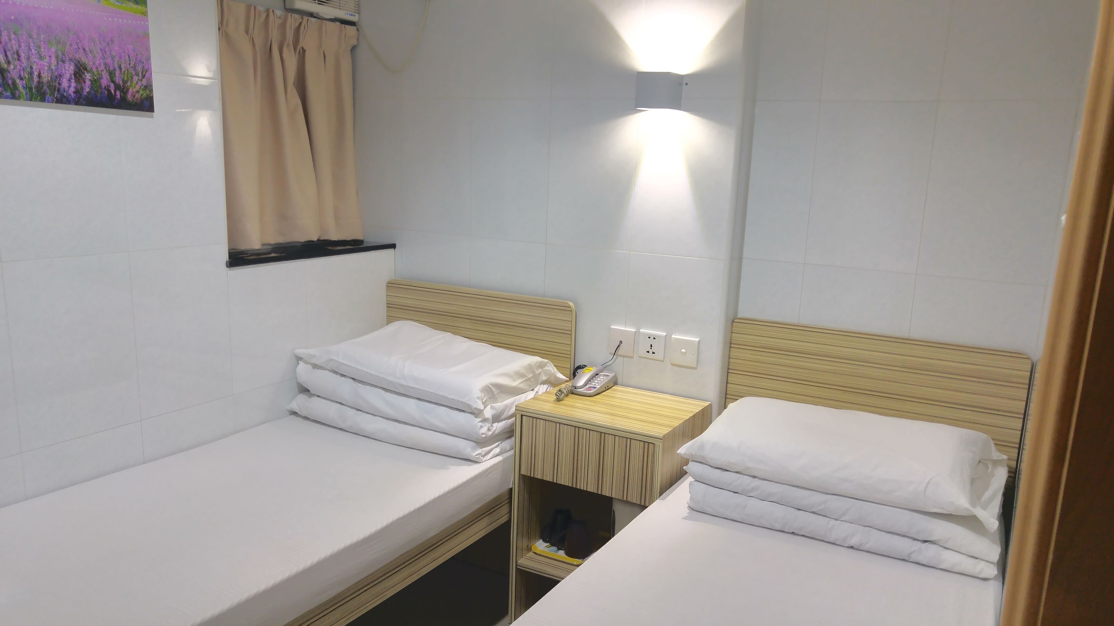 Een nette, kleine kamer met twee éénpersoonsbedden, een nachtkastje met lamp en een wandairconditioner.