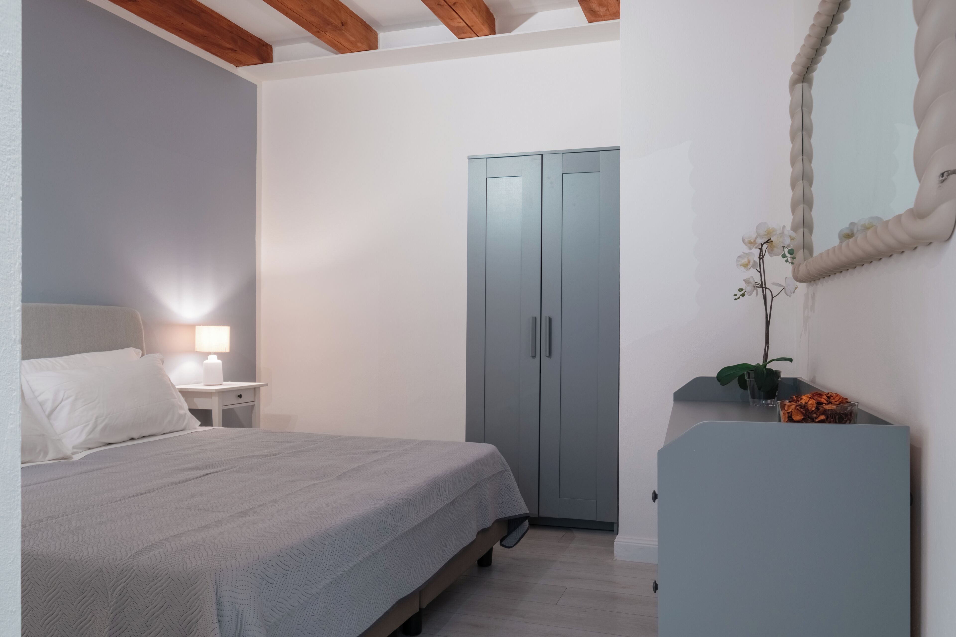 Une chambre à coucher comprenant un lit, une table de chevet, une commode, une armoire et un miroir.