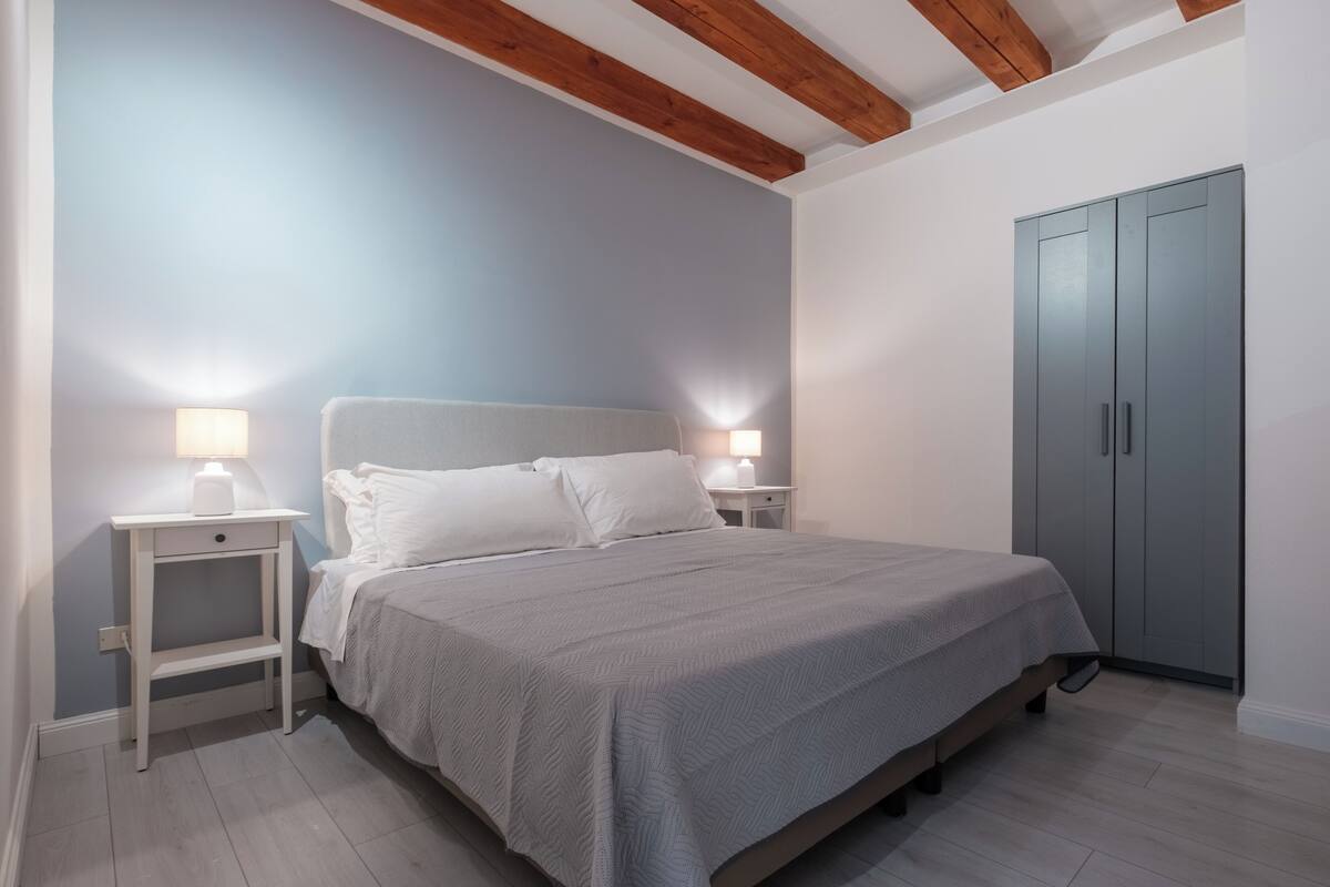 Une chambre à coucher avec un lit, des tables de chevet avec des lampes, une armoire et des poutres en bois au plafond.