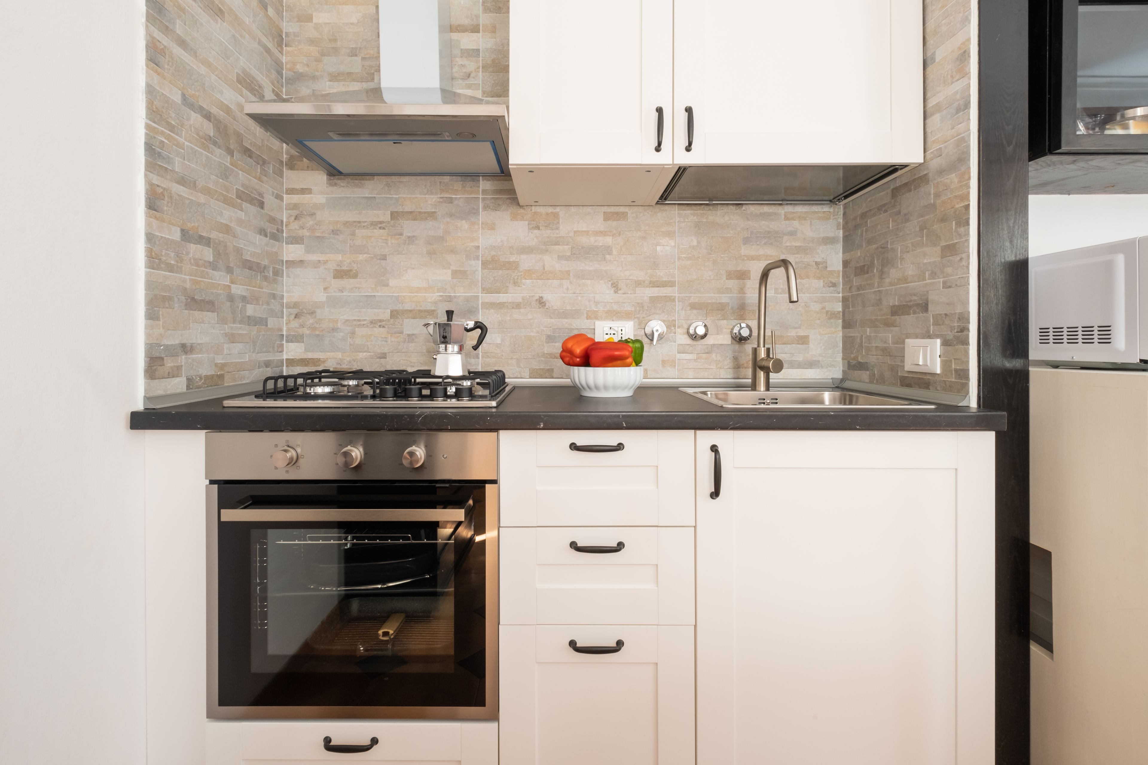 A modern kitchen with white cabinets, a black countertop, a built-in oven, a gas stove, and a sink with a faucet.