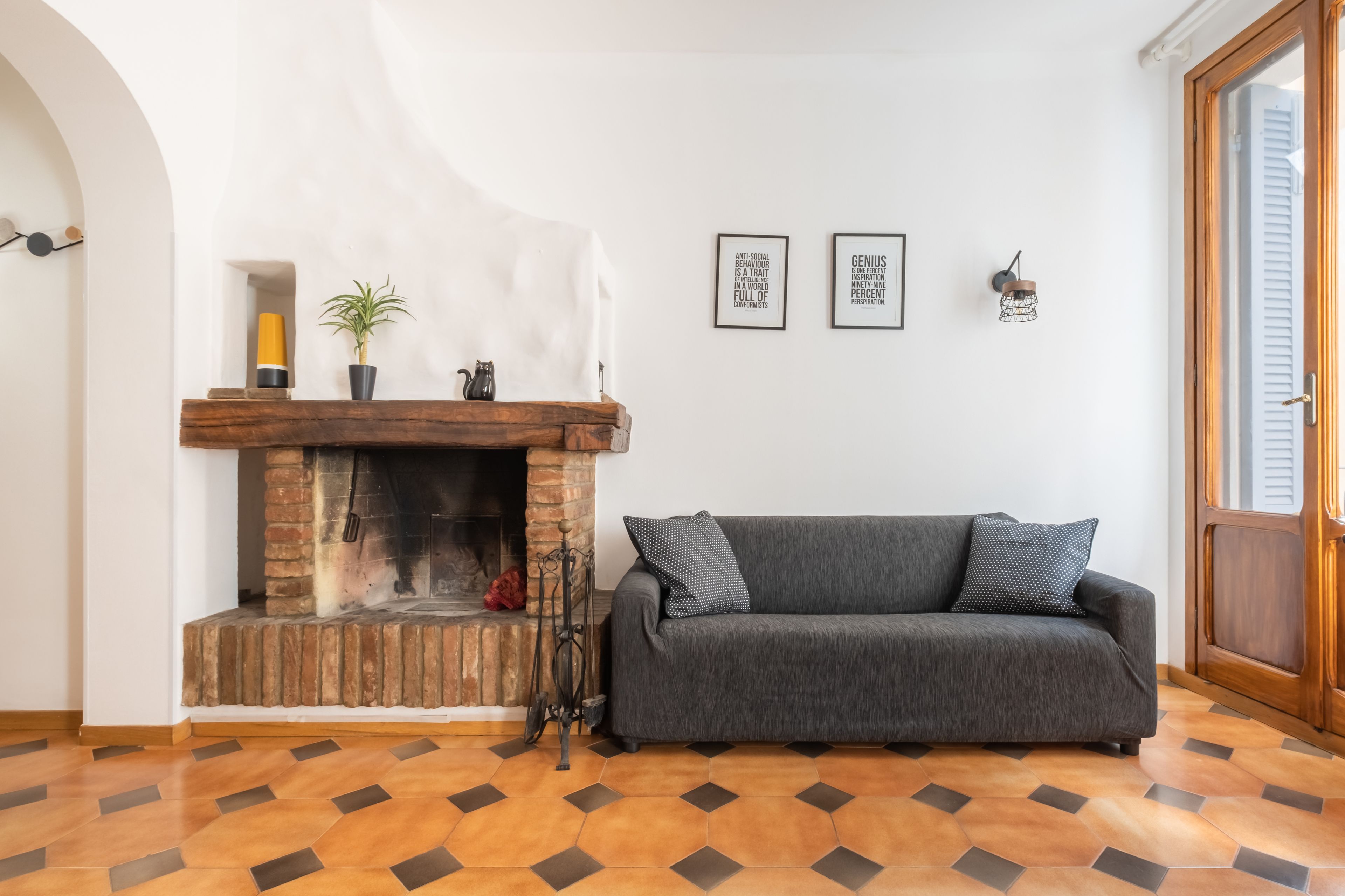 A living room with a fireplace, a grey sofa, and a patterned floor.
