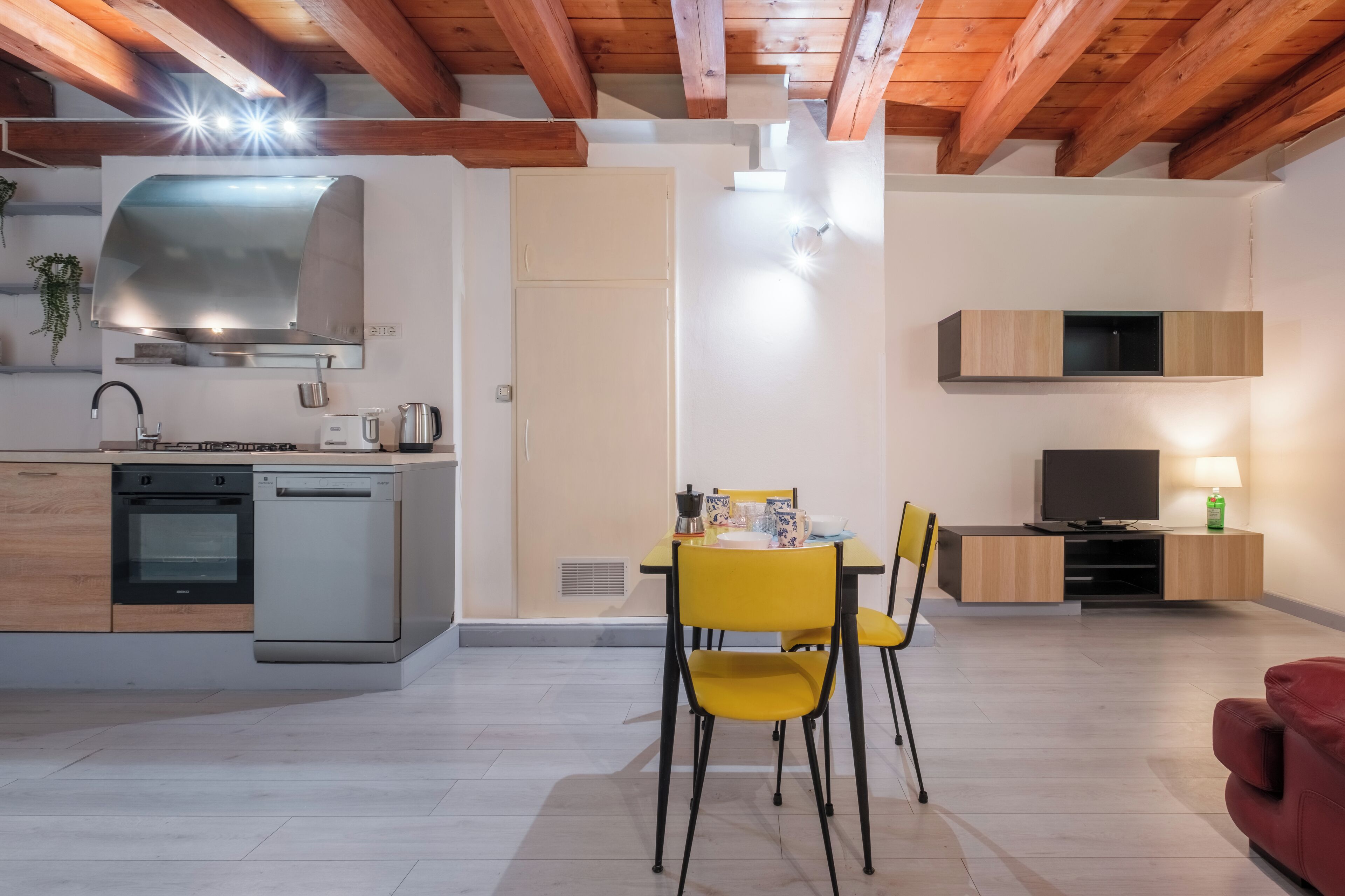 Una cucina moderna con elettrodomestici integrati, una zona pranzo con sedie gialle e un televisore in un mobile in legno.