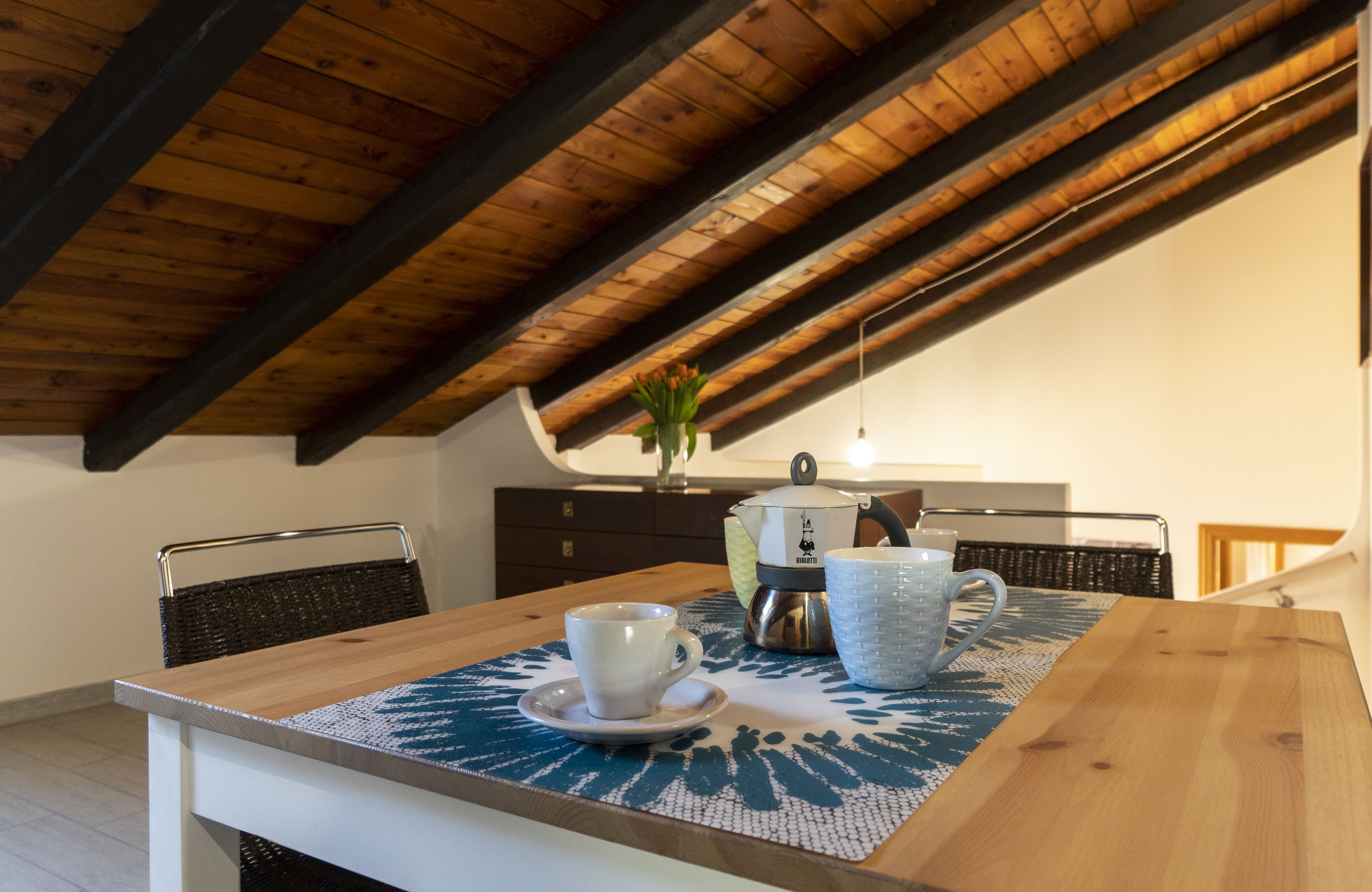 Un coin repas avec une table en bois, une tasse, un mug et une bouilloire posés sur un set de table bleu.