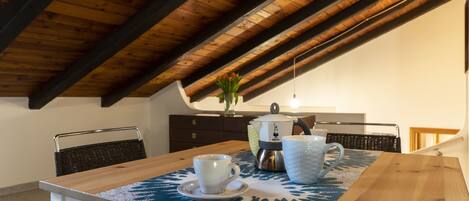 Un coin repas avec une table en bois, une tasse, un mug et une bouilloire posés sur un set de table bleu.