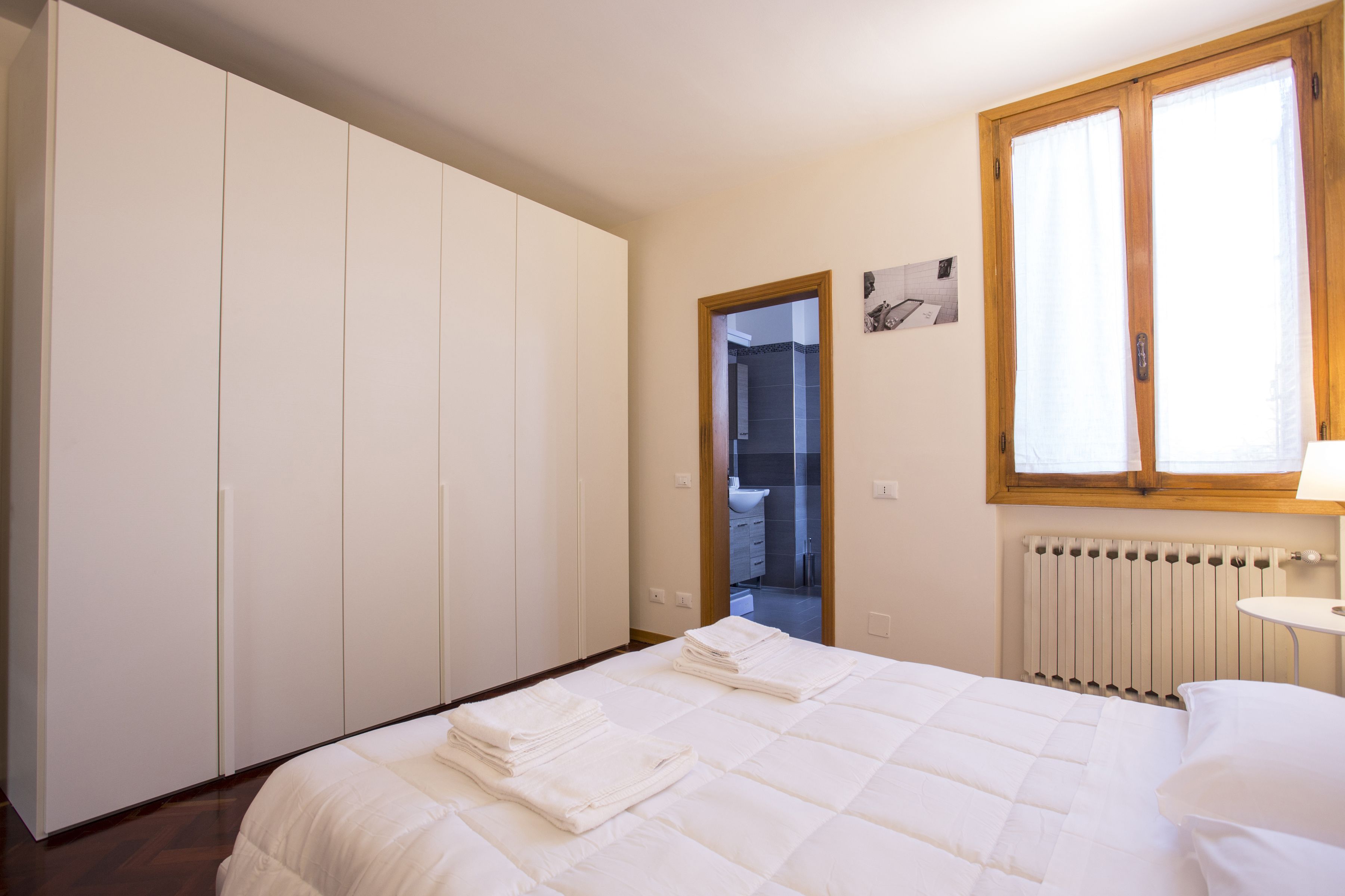 A bedroom with a bed, a wardrobe, a radiator, and a window.