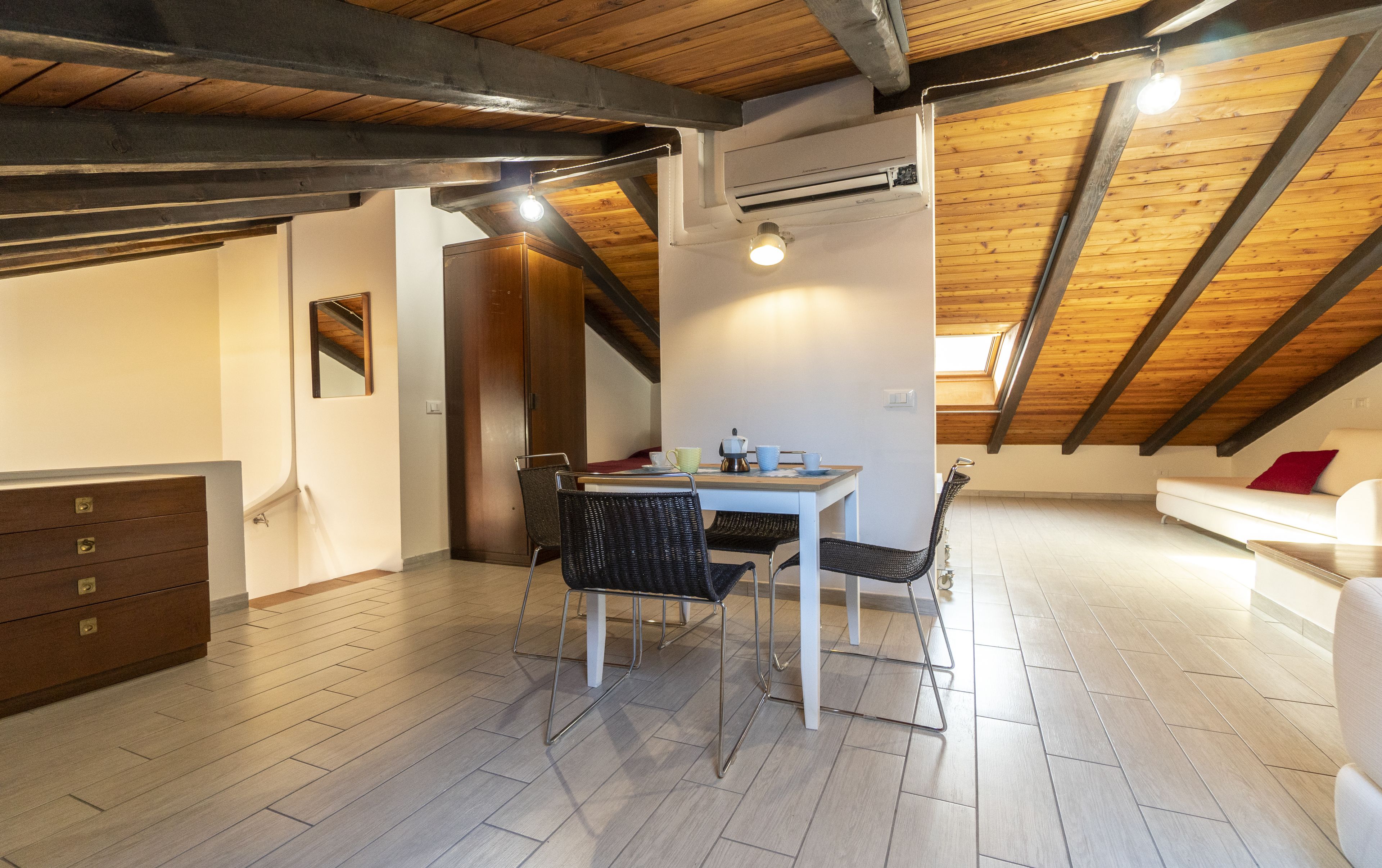Ein modernes Loft mit freiliegenden Holzbalken, einem Essbereich mit Tisch und Stühlen, einer Couch und einer Kommode.