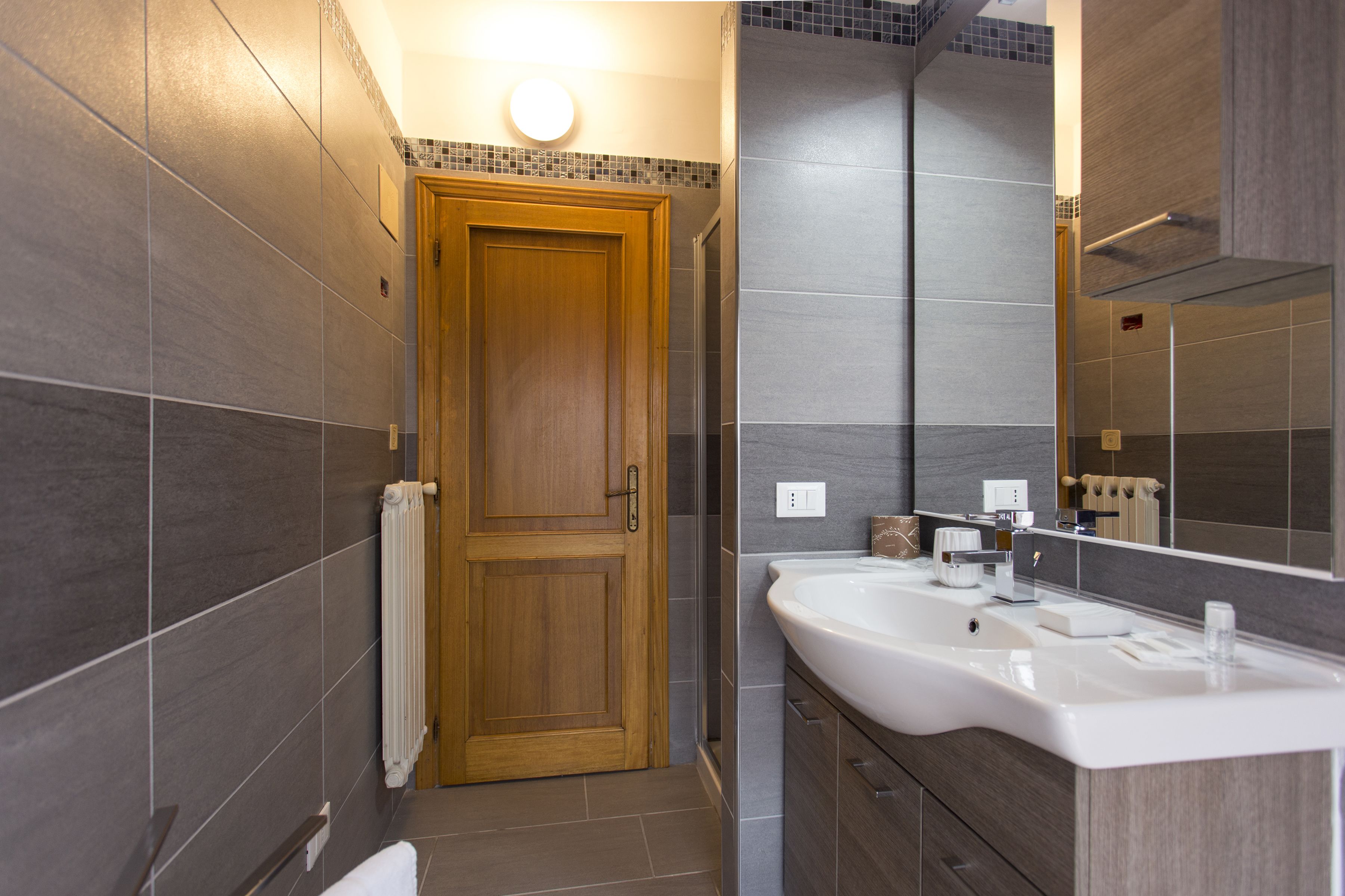 A modern bathroom with a wooden door, a large mirror, and a white sink.