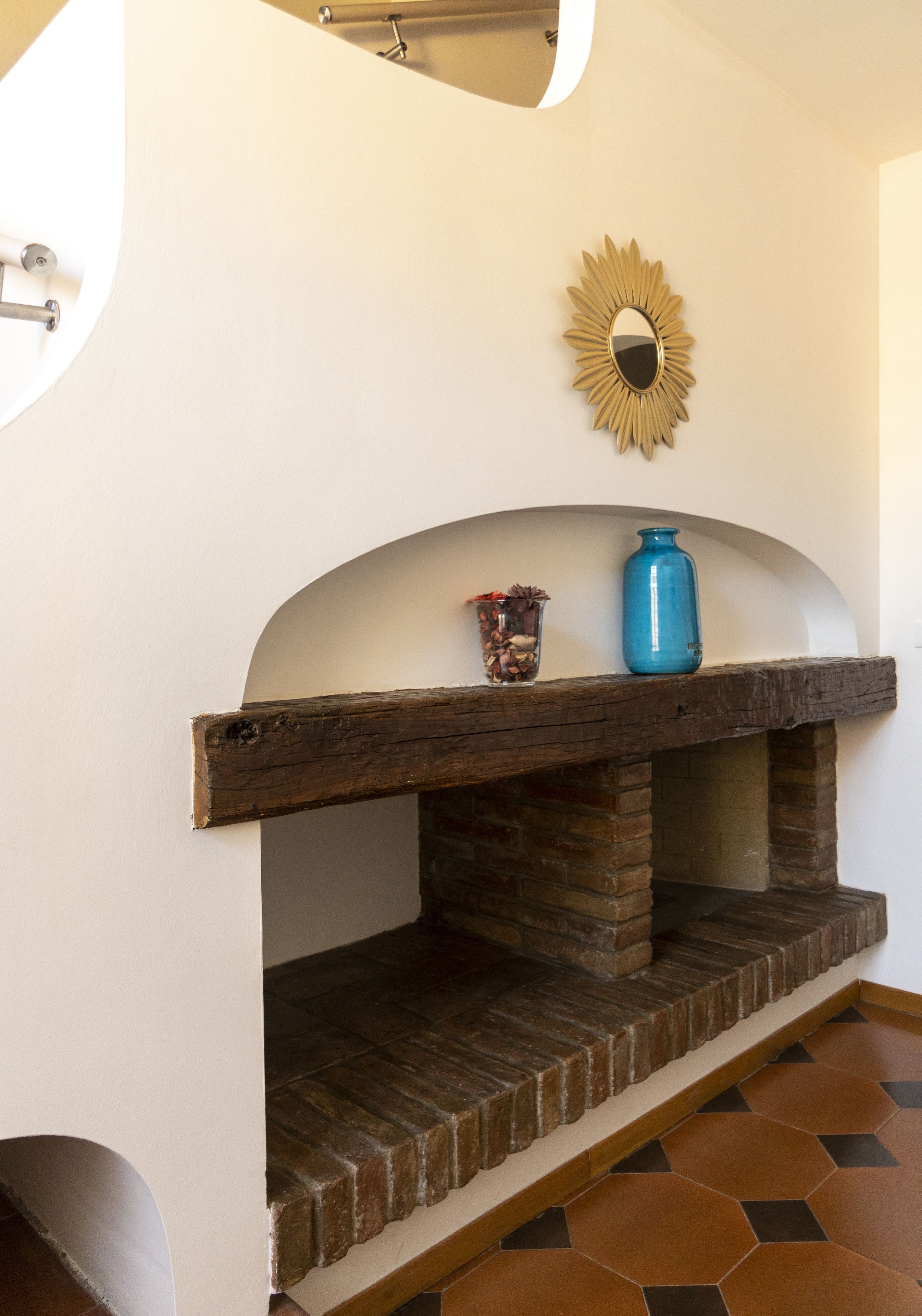 Une cheminée au décor rustique en briques, un vase bleu et un miroir décoratif accroché au mur.