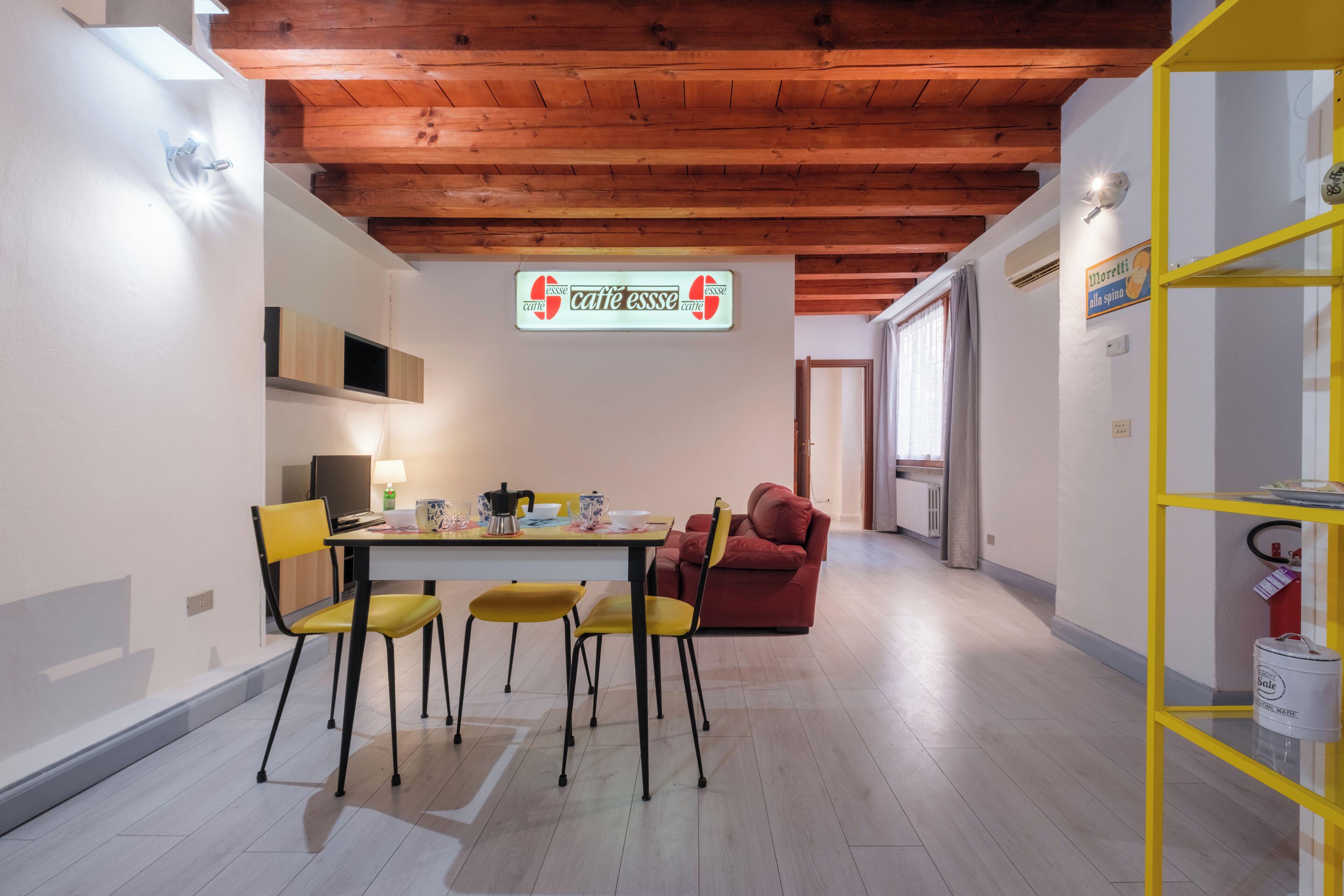 Un comedor con techo de madera, una mesa con sillas y un estante amarillo.