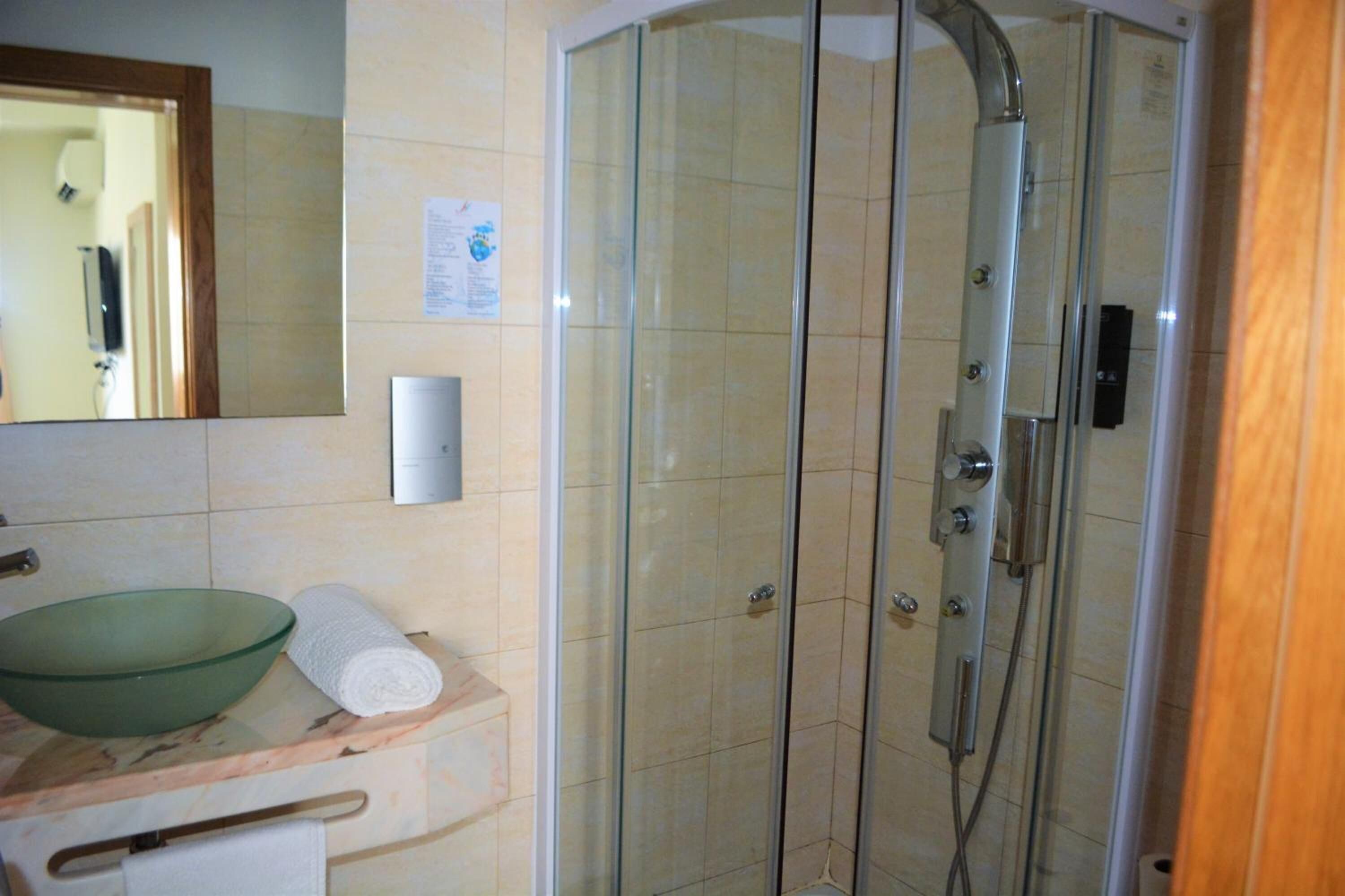 A bathroom with a glass-enclosed shower, a green glass bowl, and a towel on the counter.