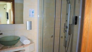 A bathroom with a glass-enclosed shower, a green glass bowl, and a towel on the counter.