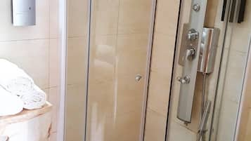 A glass-enclosed shower stall with a handheld showerhead and a wall-mounted faucet.