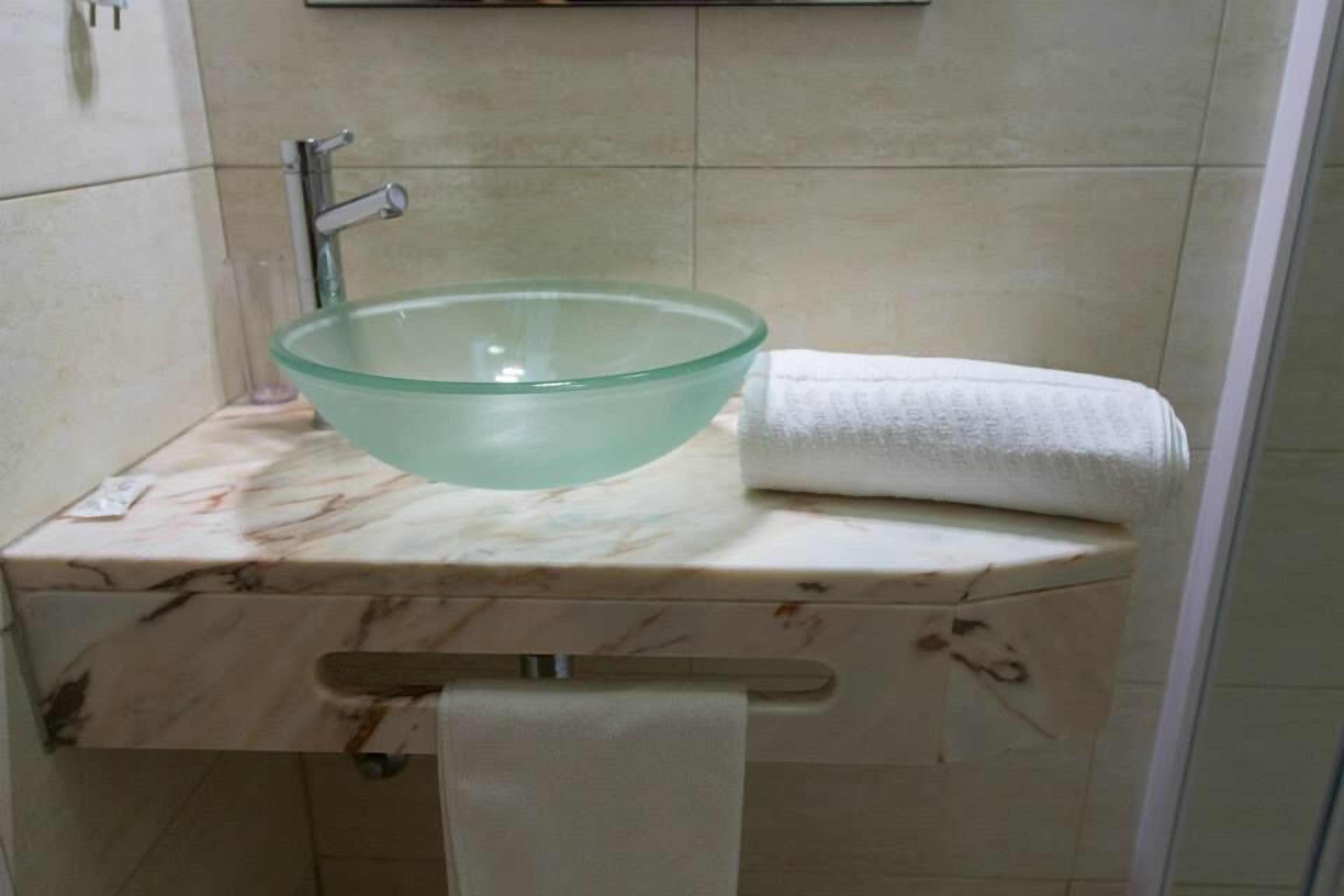 Un baño con un lavabo de vidrio, una toalla y encimera de mármol.