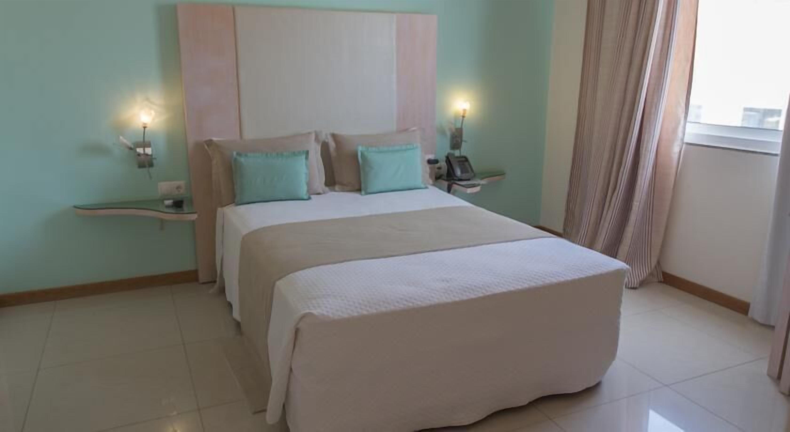 Habitación de hotel con una cama grande, dos mesitas de noche y un ventanal con cortinas.