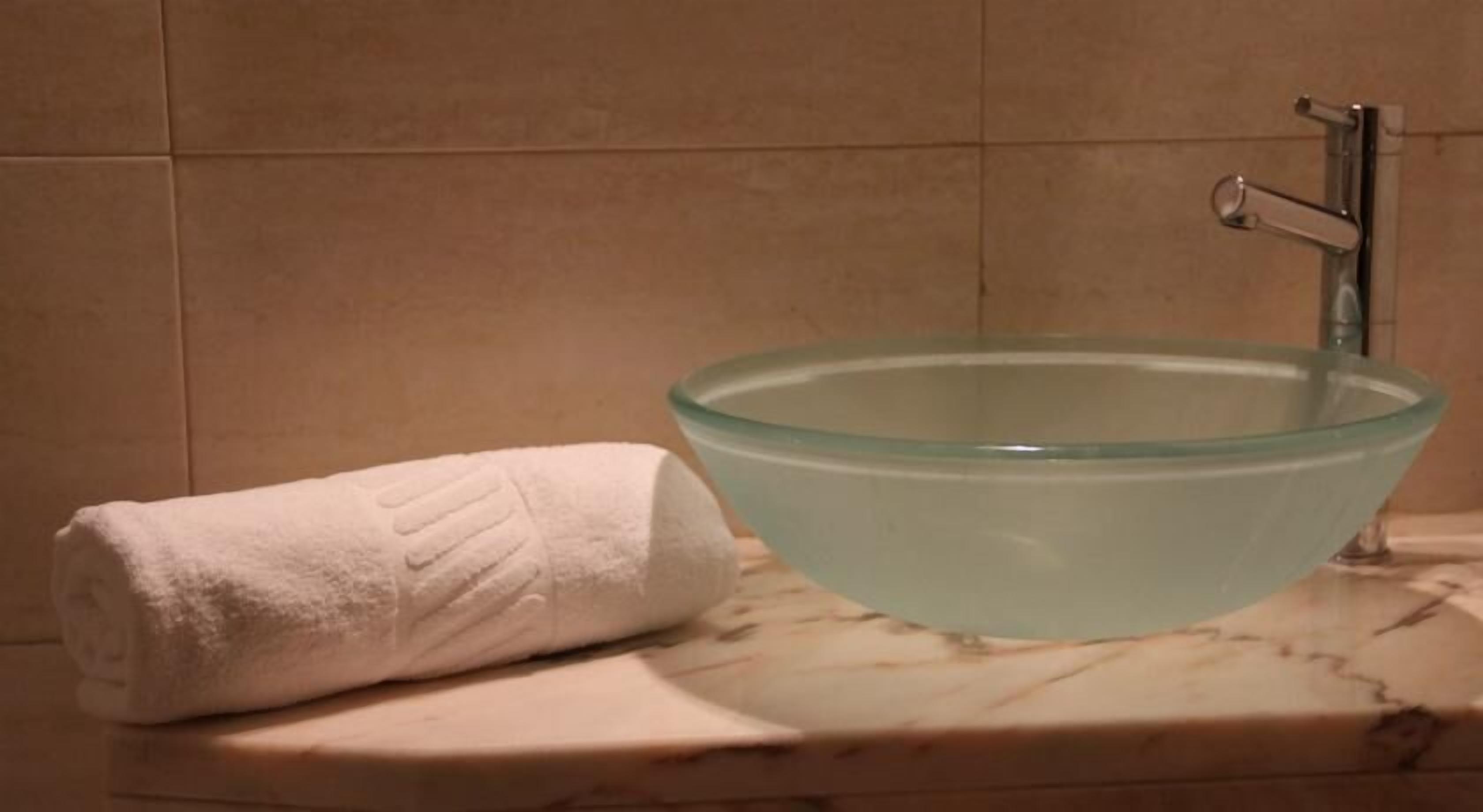Ett badrum med ett handfat i form av en glasskål, en vit handduk och en bänkskiva i marmor.