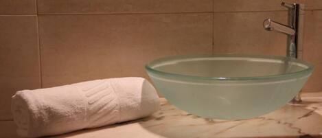A bathroom with a glass bowl sink, a white towel, and a marble countertop.