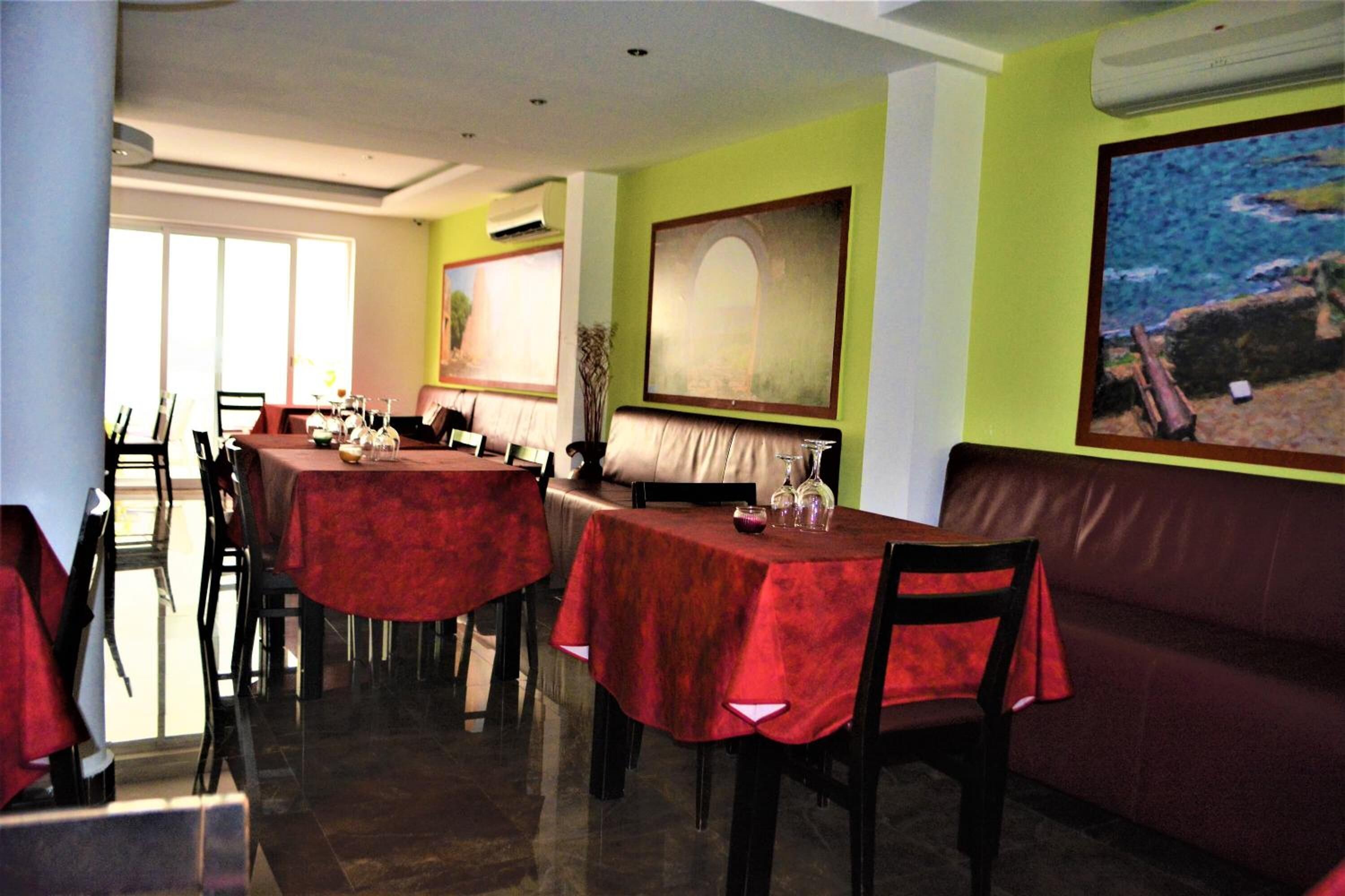 Un comedor con mesas cubiertas con manteles rojos, un banco de cuero y obras de arte en las paredes.