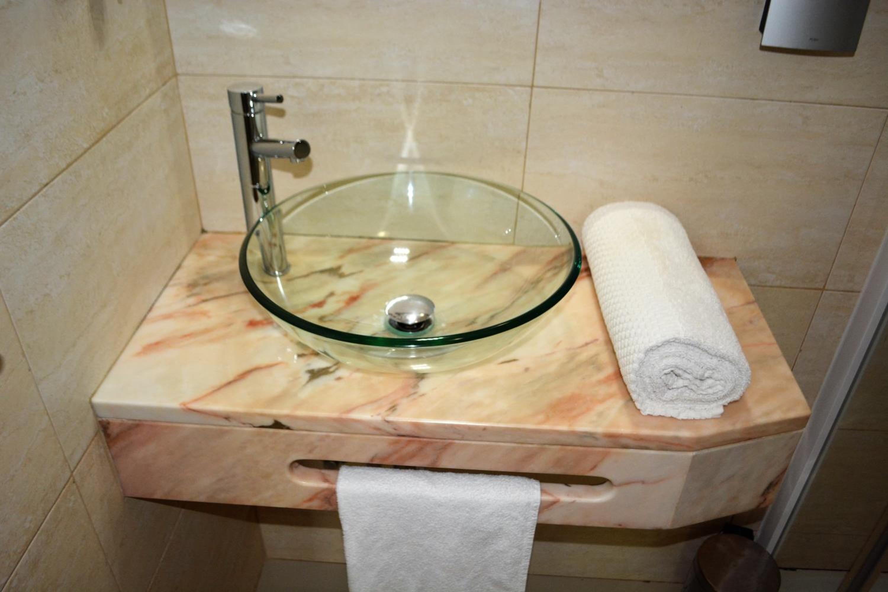 Un baño con un lavabo de cristal, una toalla y encimera de mármol.