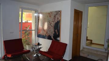 Una sala de estar moderna con un sofá rojo, una mesa de centro de vidrio y un cuadro abstracto grande en la pared.