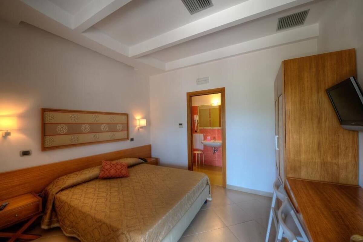 Una habitación de hotel con cama, mesita de noche y televisor montado en la pared.