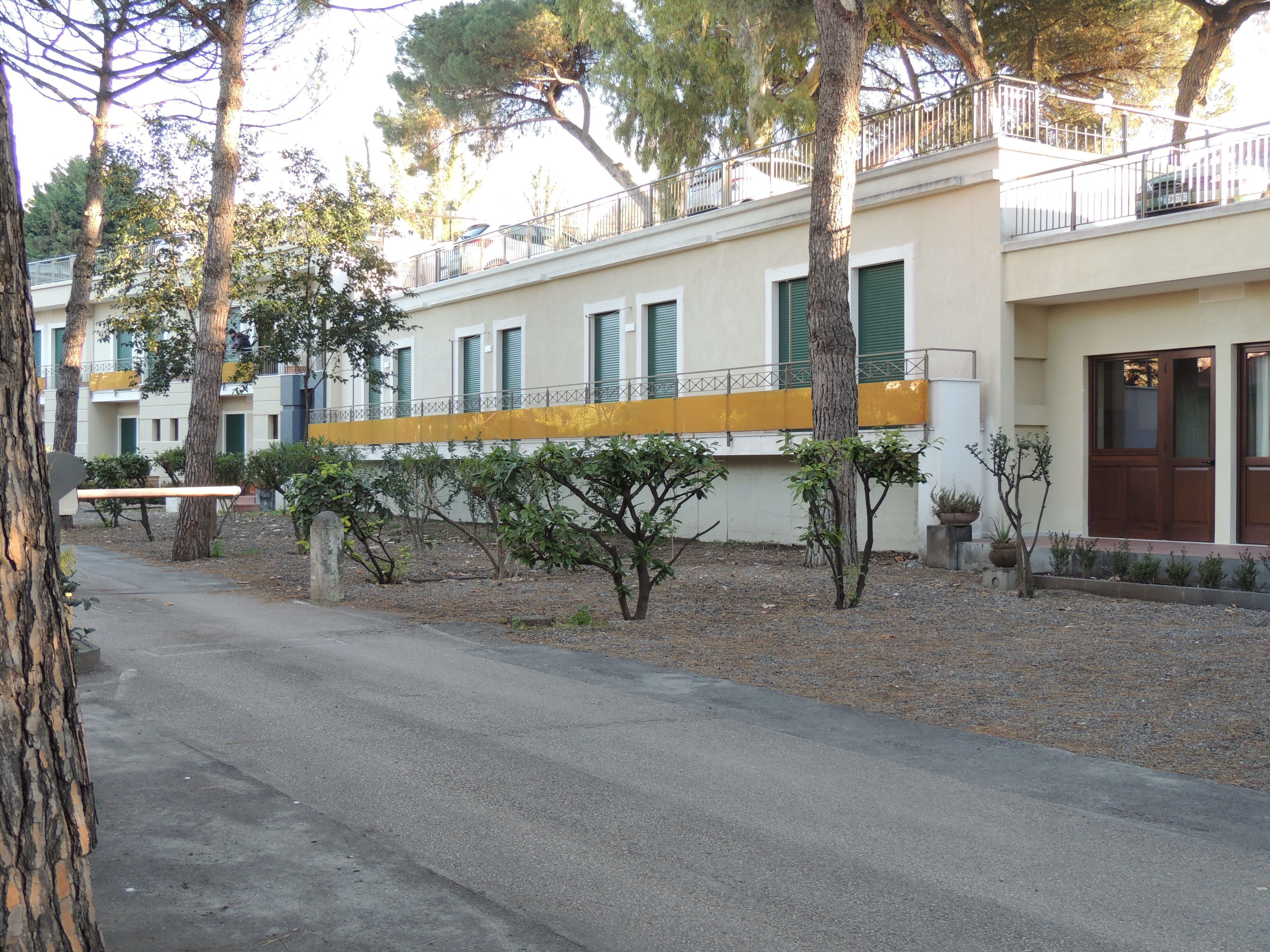 A building with a yellow balcony, trees, and a paved road.