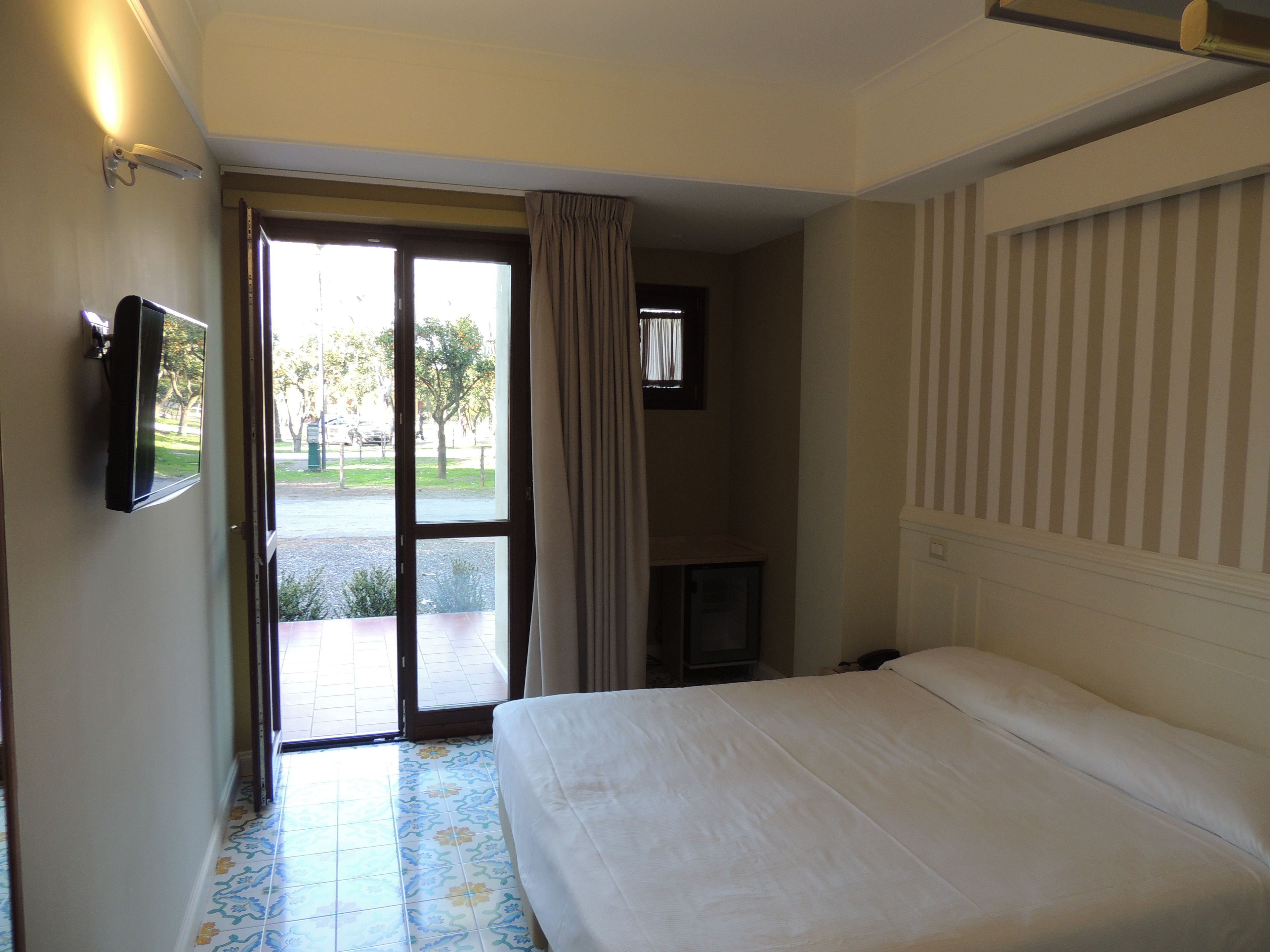A hotel room with a bed, a television, a window with curtains, and a view of the outside.