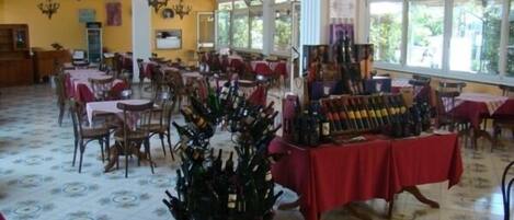 A spacious dining area with tables and chairs, a wine display, and large windows allowing natural light.