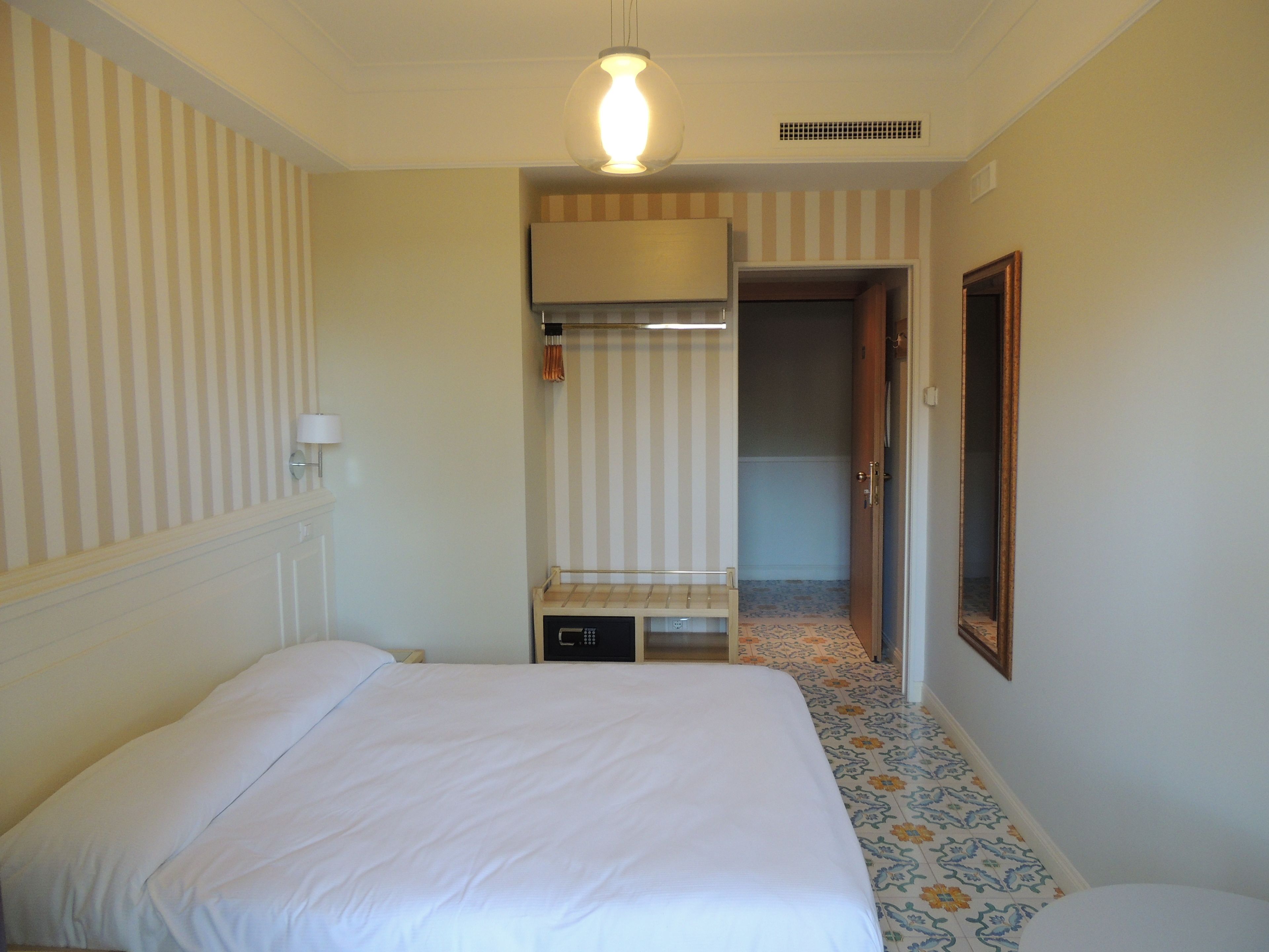 A hotel room with a bed, a small desk, a mirror, and a door leading to another room.