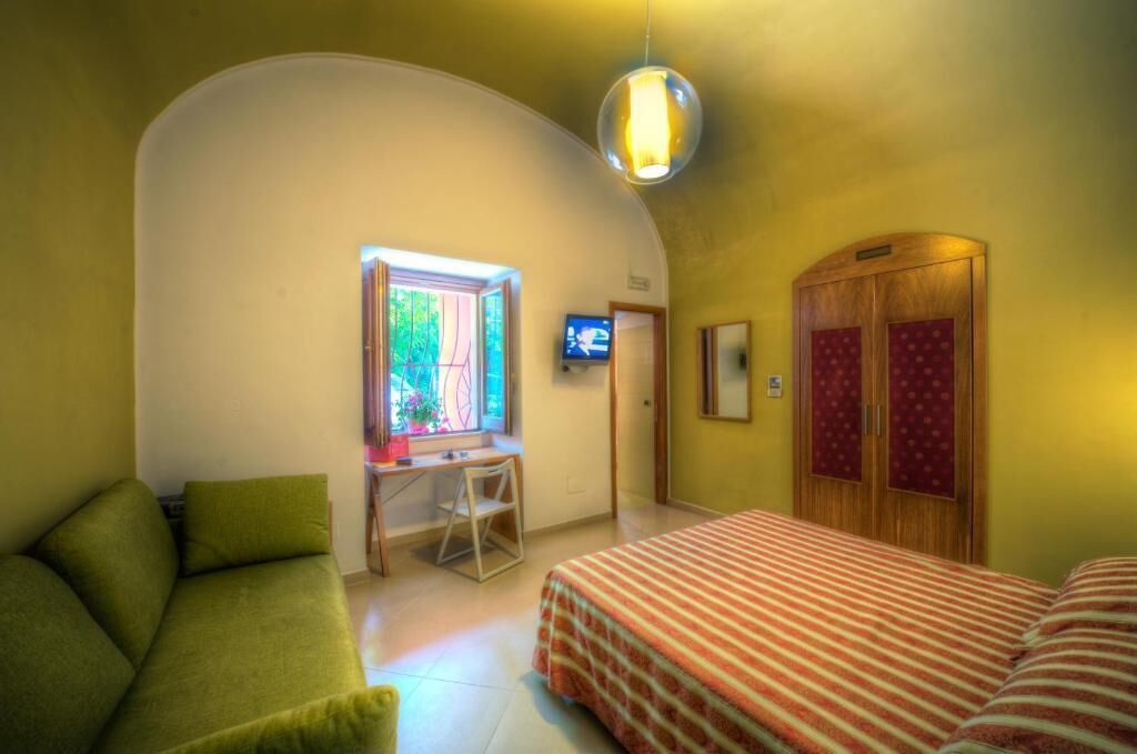 Una habitación con una pared curva, un escritorio con una silla, una cama con colcha a rayas y un televisor en la pared.