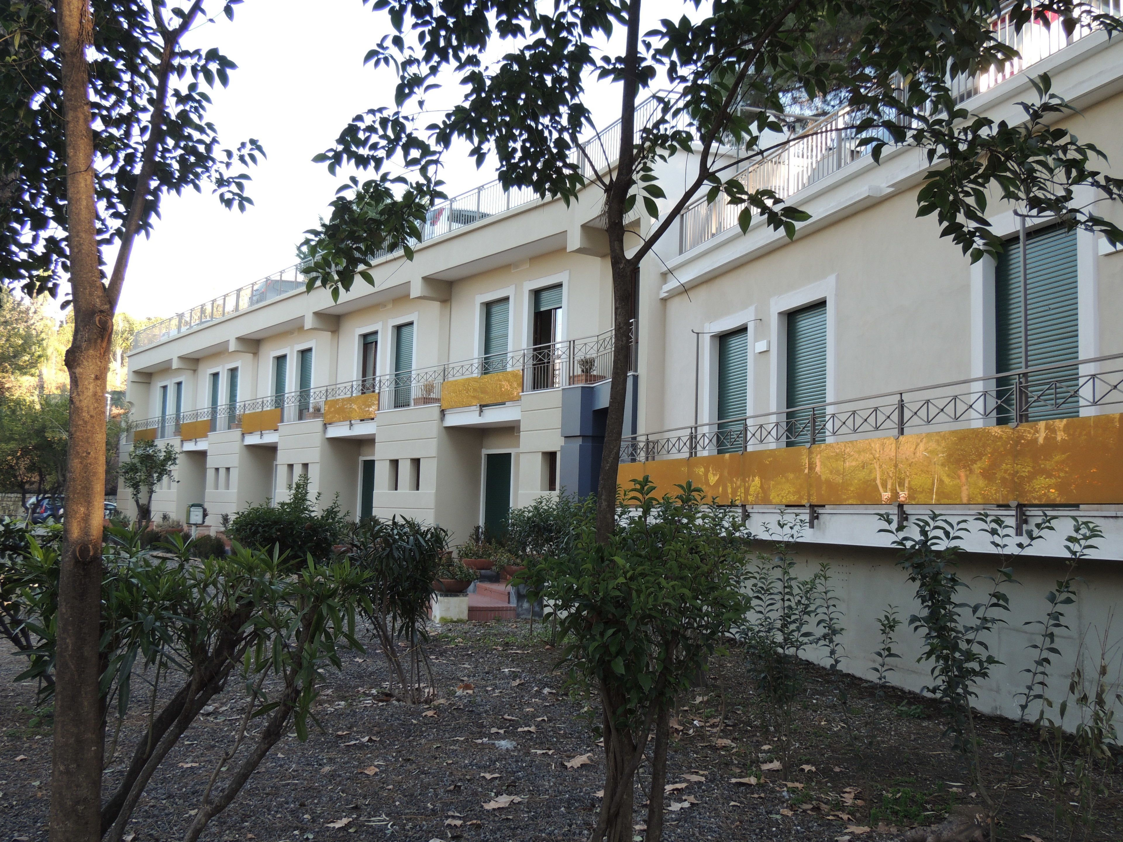 A row of multi-story buildings with balconies, surrounded by trees and shrubs.